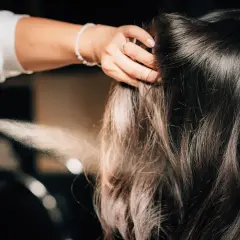 Hårstylist stylar axellångt hår med hårspray.