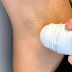 En hand med rosa naglar applicerar antiperspirant deo under armen.