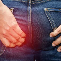 En person i jeans kliar sig i rumpan, med en röd glöd som indikerar obehag.