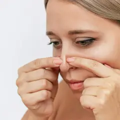 En kvinna använder fingrarna för att ta bort inkapslade pormaskar på näsan.