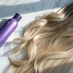 Lila flaska bredvid blont hår. Perfekt för att få bort gula toner i håret och ge det en kallare nyans.