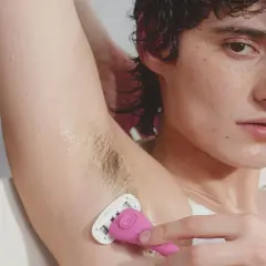 Close-up of a person shaving their armpit with a pink razor.
