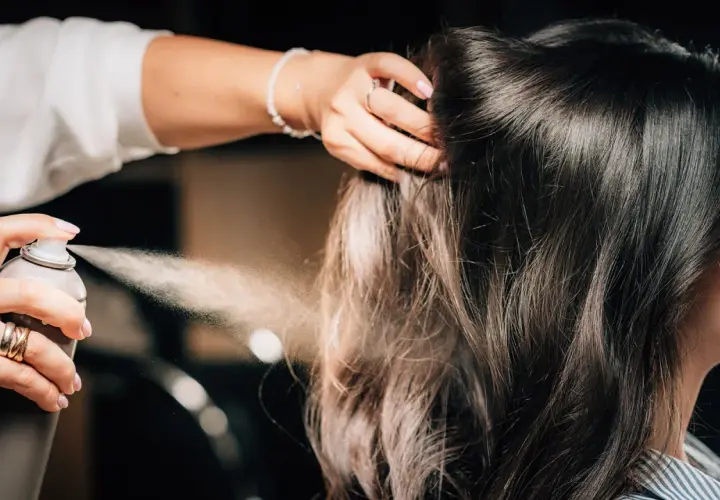 Hårstylist stylar axellångt hår med hårspray.