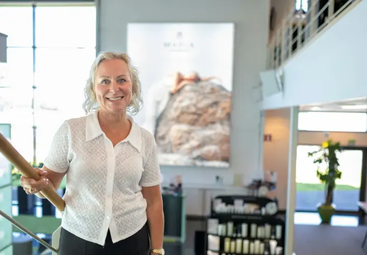 En kvinna ler vid en trappa. Bakom henne syns en stor bild med texten "MARIA ÅKERBERG".