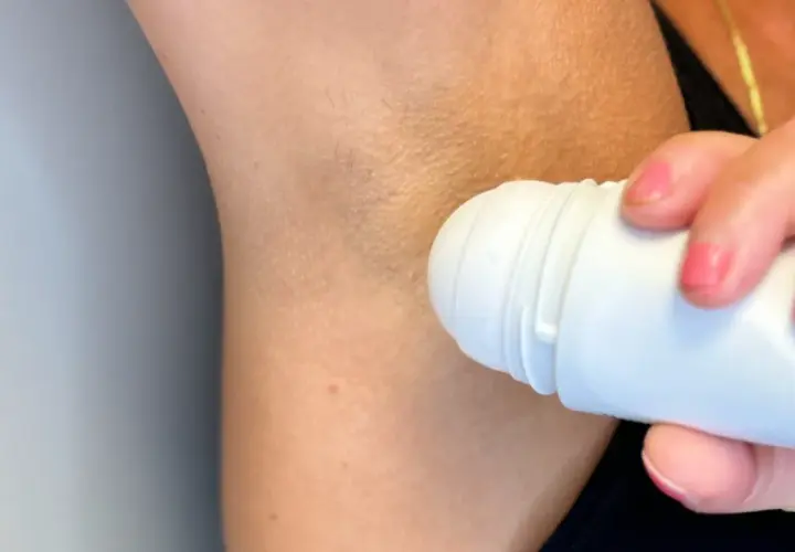 En hand med rosa naglar applicerar antiperspirant deo under armen.