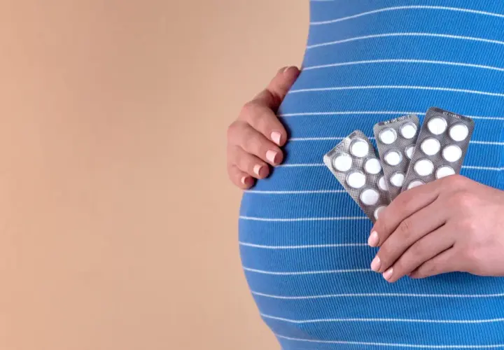 Gravid kvinna håller upp tre paket med tabletter, troligen gravid vitaminer, mot sin mage.