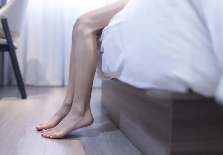 En person sitter på sängkanten, benen dinglar. Kanske en huskur mot restless legs kan ge ro.