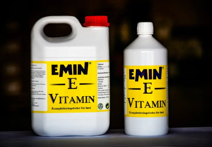 Två flaskor med hästfoder som innehåller vitamin E. Den större flaskan har ett rött lock, den mindre ett vitt.