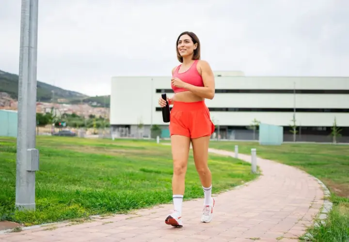 Kvinna joggar på en stig med en vattenflaska i handen, ett steg mot att gå ner i vikt.