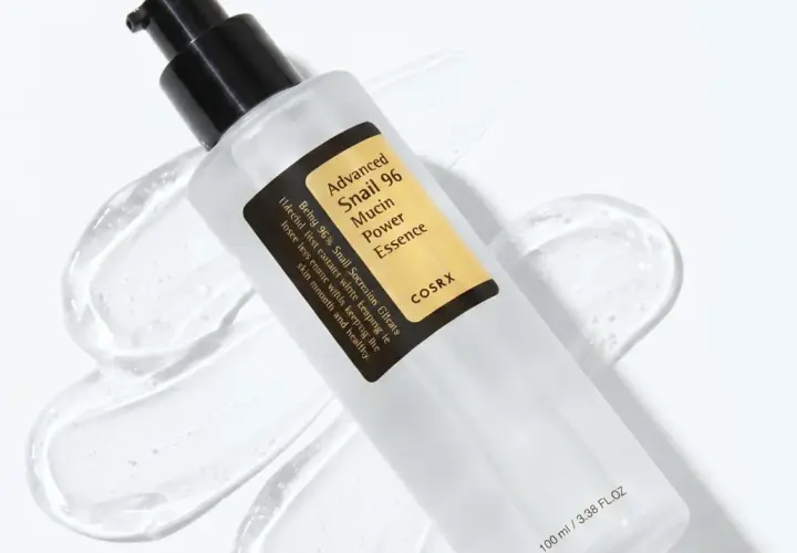 En flaska med COSRX Advanced Snail 96 Mucin Power Essence, en populär produkt inom snigelslem hudvård, omgiven av dess klara, geléaktiga konsistens.
