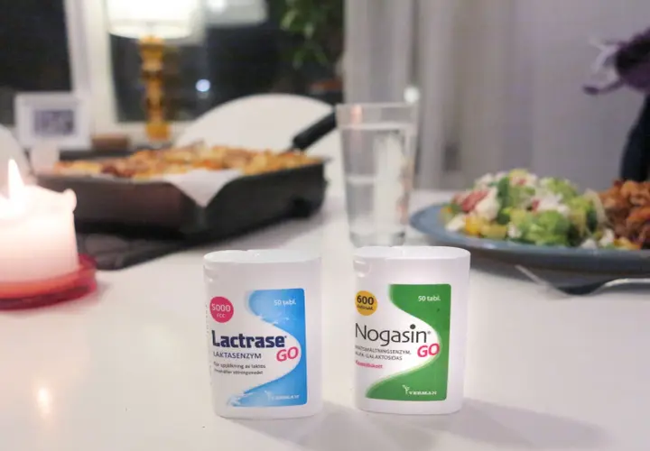 Två förpackningar laktos tabletter, Lactrase och Nogasin, står på ett bord med mat i bakgrunden.