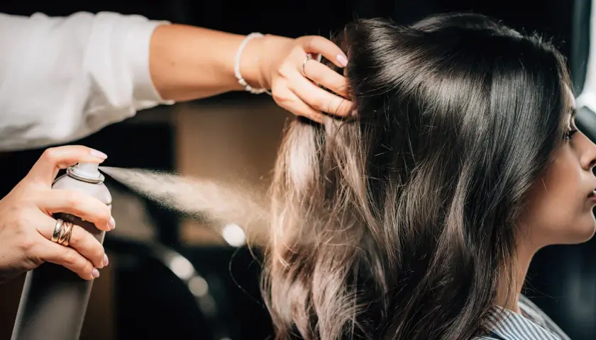 Hårstylist stylar axellångt hår med hårspray.