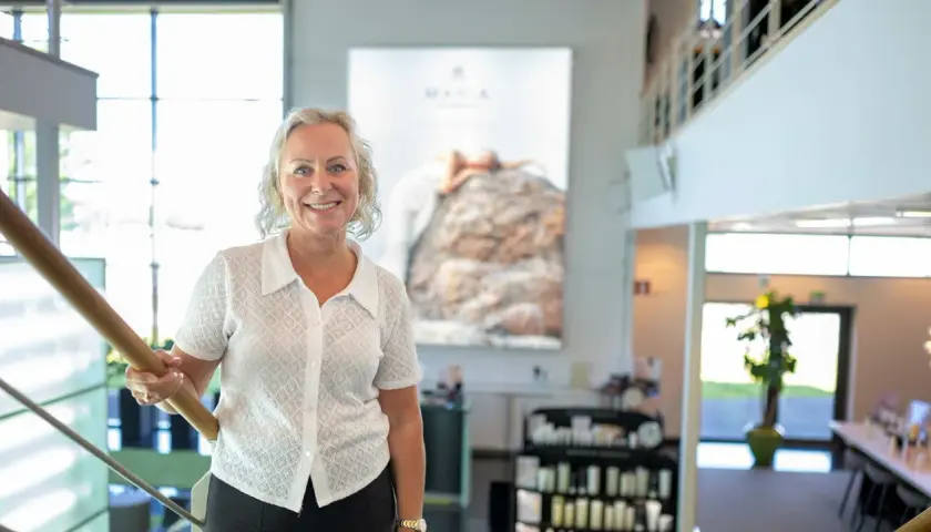 En kvinna ler vid en trappa. Bakom henne syns en stor bild med texten "MARIA ÅKERBERG".