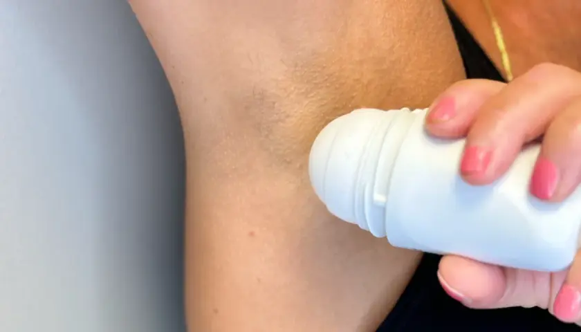 En hand med rosa naglar applicerar antiperspirant deo under armen.