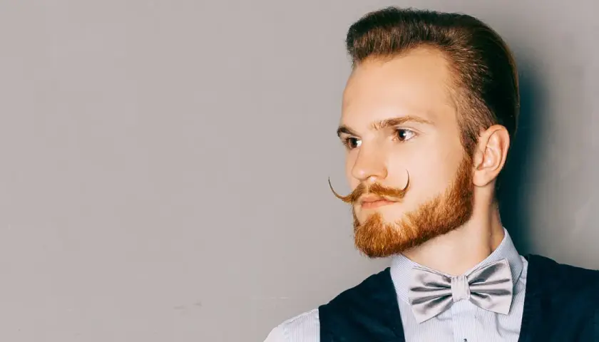 Man med imponerande mustasch stilar, en elegant fluga och en snygg frisyr.