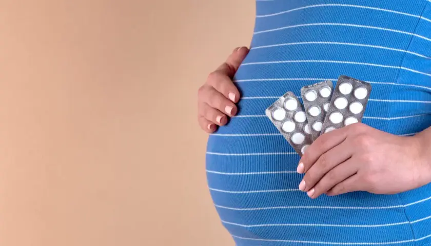 Gravid kvinna håller upp tre paket med tabletter, troligen gravid vitaminer, mot sin mage.