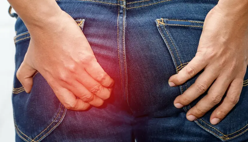En person i jeans kliar sig i rumpan, med en röd glöd som indikerar obehag.