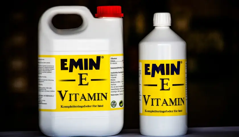 Två flaskor med hästfoder som innehåller vitamin E. Den större flaskan har ett rött lock, den mindre ett vitt.