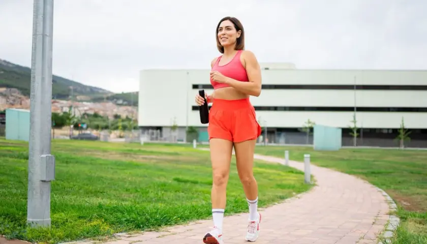 Kvinna joggar på en stig med en vattenflaska i handen, ett steg mot att gå ner i vikt.