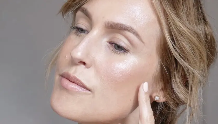 En kvinna med glansig hud och en lätt makeup, som visar upp sin fräscha hy.