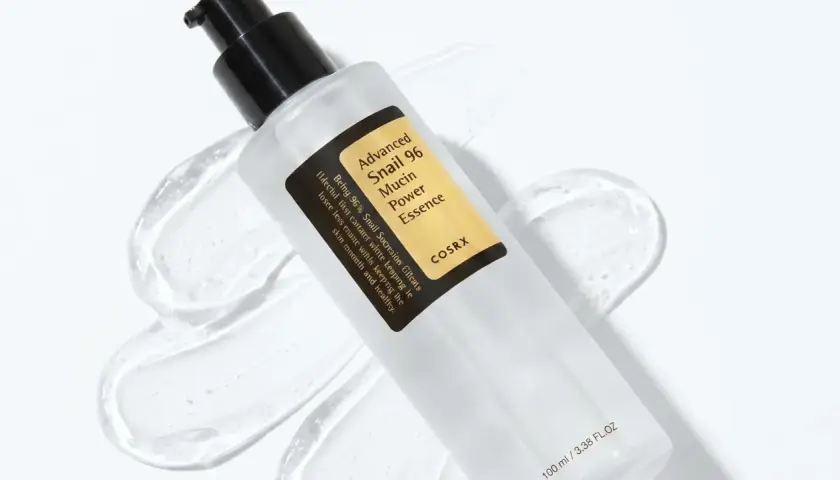 En flaska med COSRX Advanced Snail 96 Mucin Power Essence, en populär produkt inom snigelslem hudvård, omgiven av dess klara, geléaktiga konsistens.