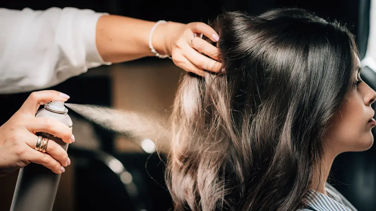 Hårstylist stylar axellångt hår med hårspray.