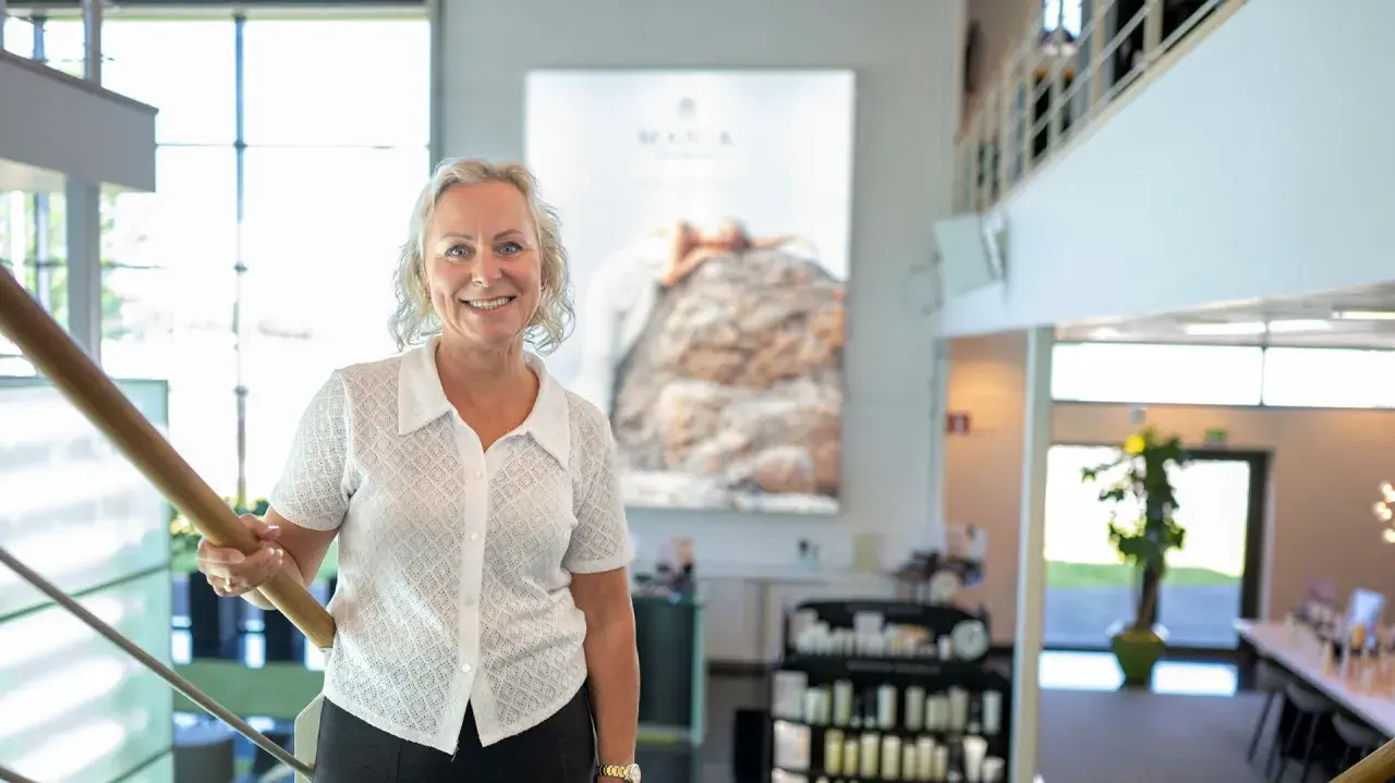 En kvinna ler vid en trappa. Bakom henne syns en stor bild med texten "MARIA ÅKERBERG".