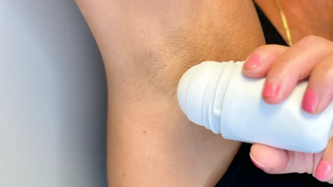 En hand med rosa naglar applicerar antiperspirant deo under armen.
