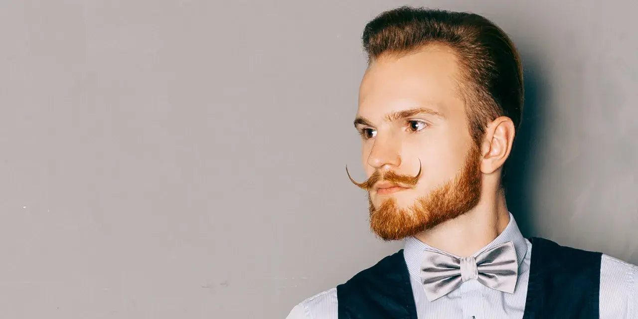 Man med imponerande mustasch stilar, en elegant fluga och en snygg frisyr.