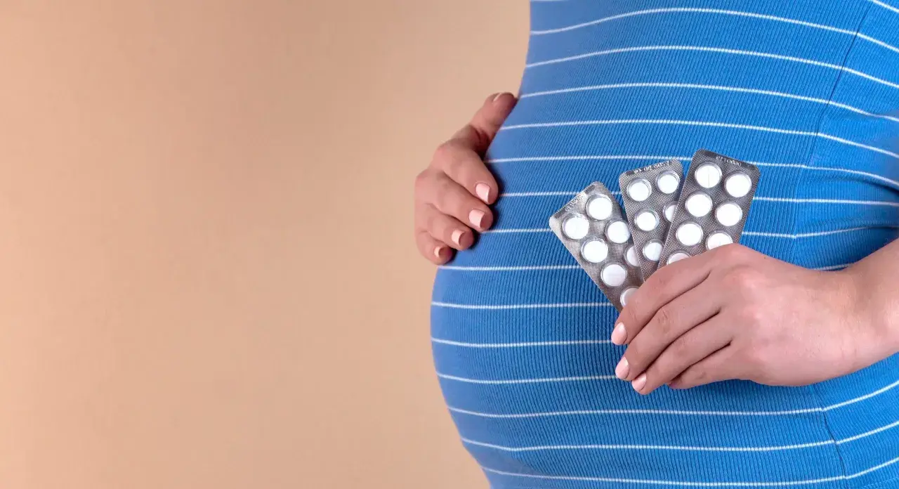 Gravid kvinna håller upp tre paket med tabletter, troligen gravid vitaminer, mot sin mage.