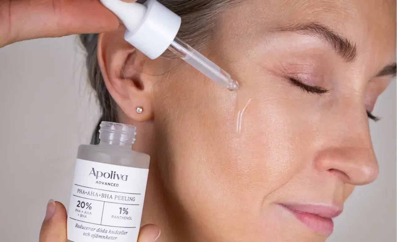 En droppe hudvård med aha syra appliceras på ansiktet. Flaskan visar "PHA+AHA+BHA PEELING".