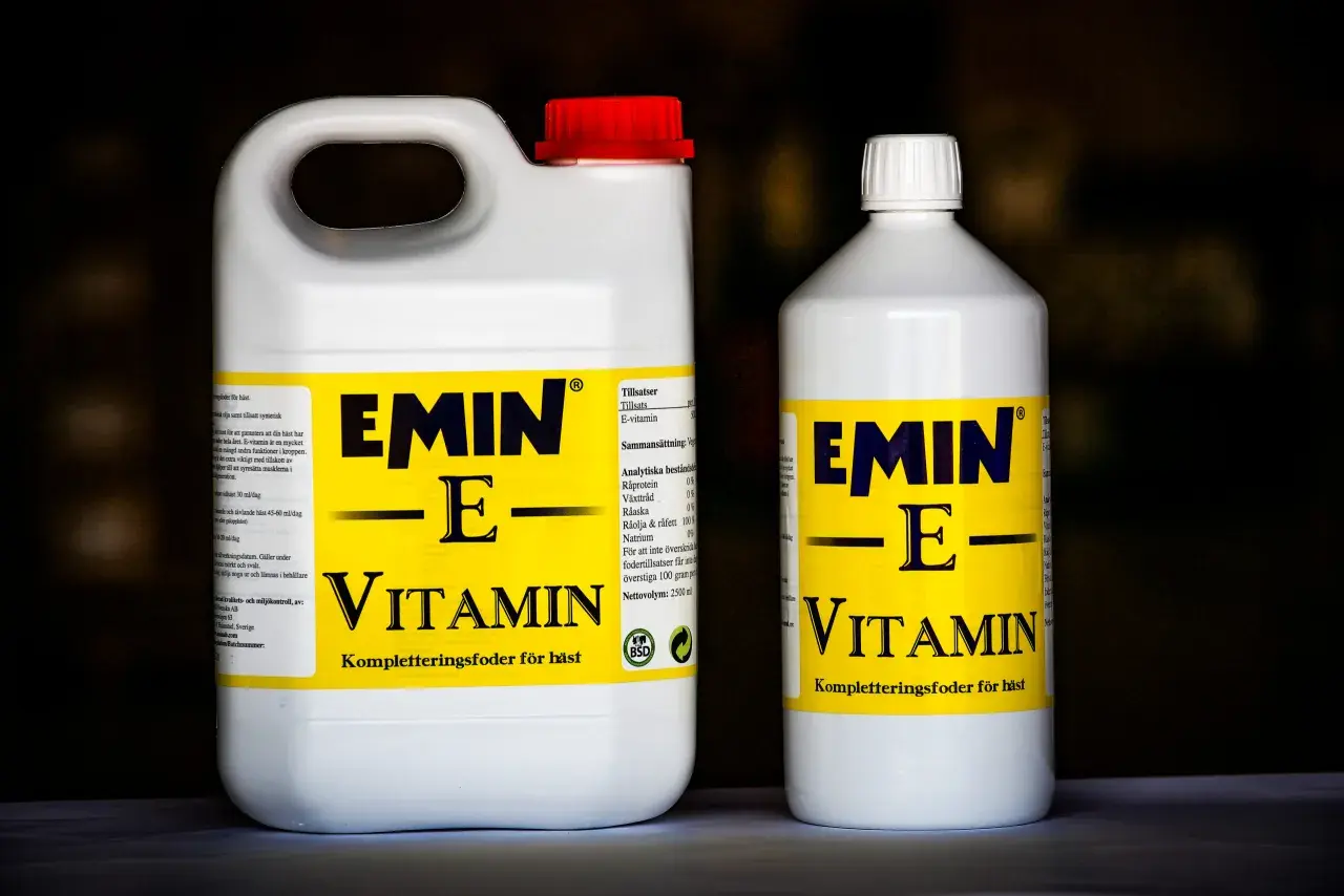 Två flaskor med hästfoder som innehåller vitamin E. Den större flaskan har ett rött lock, den mindre ett vitt.