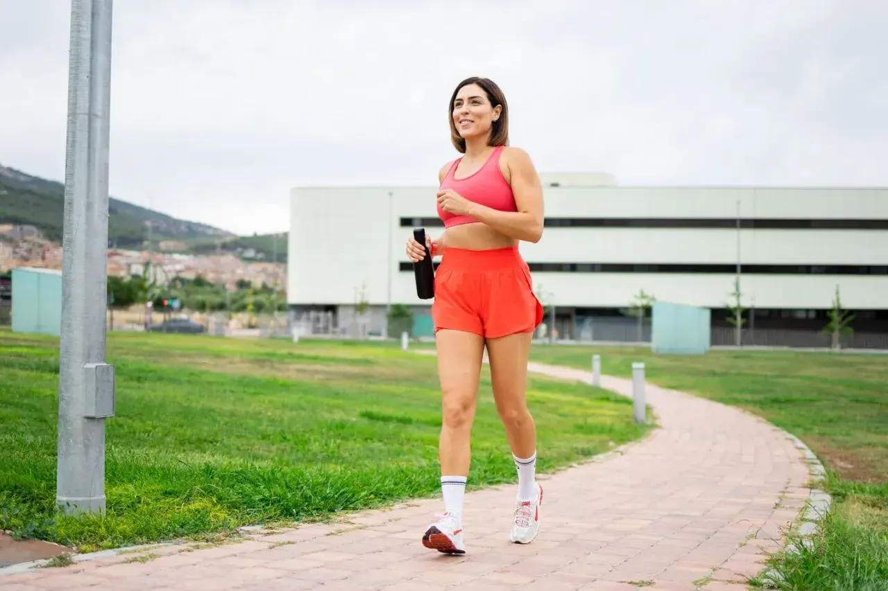Kvinna joggar på en stig med en vattenflaska i handen, ett steg mot att gå ner i vikt.