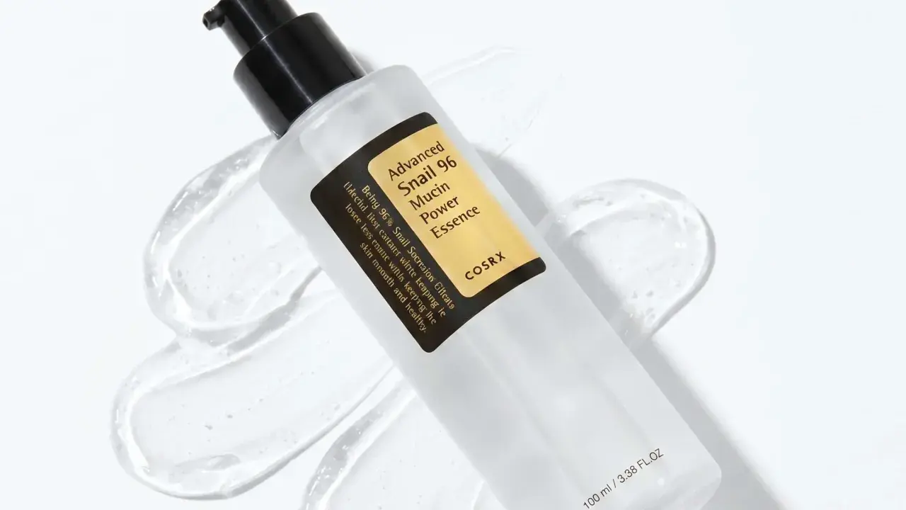 En flaska med COSRX Advanced Snail 96 Mucin Power Essence, en populär produkt inom snigelslem hudvård, omgiven av dess klara, geléaktiga konsistens.