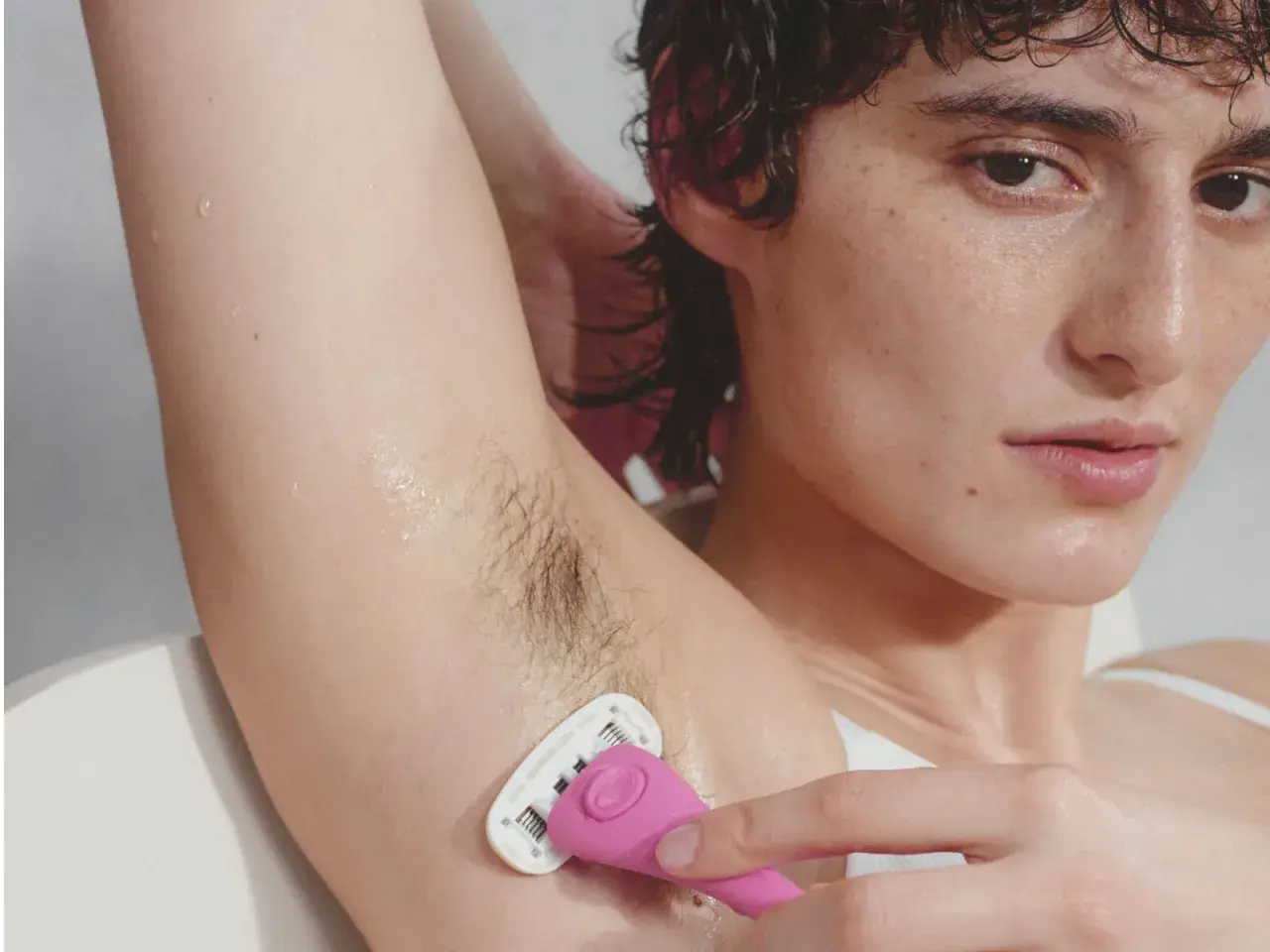 Close-up of a person shaving their armpit with a pink razor.